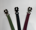 Three webbing straps in green, black, and purple with metal clasps on a white background.