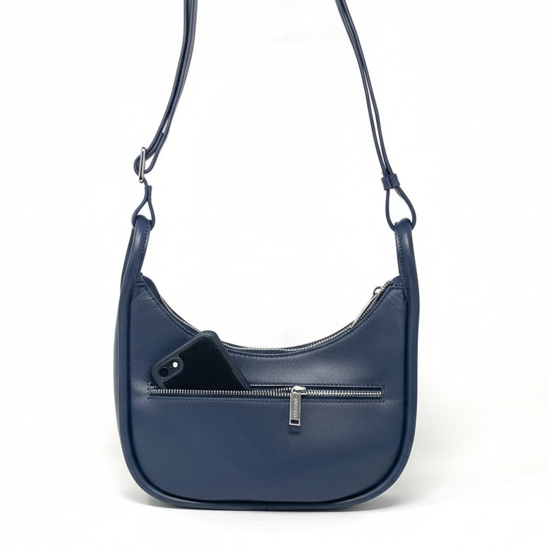 Back view of Sabrina navy blue leather crossbody bag showing exterior zipper pocket with a phone inside.