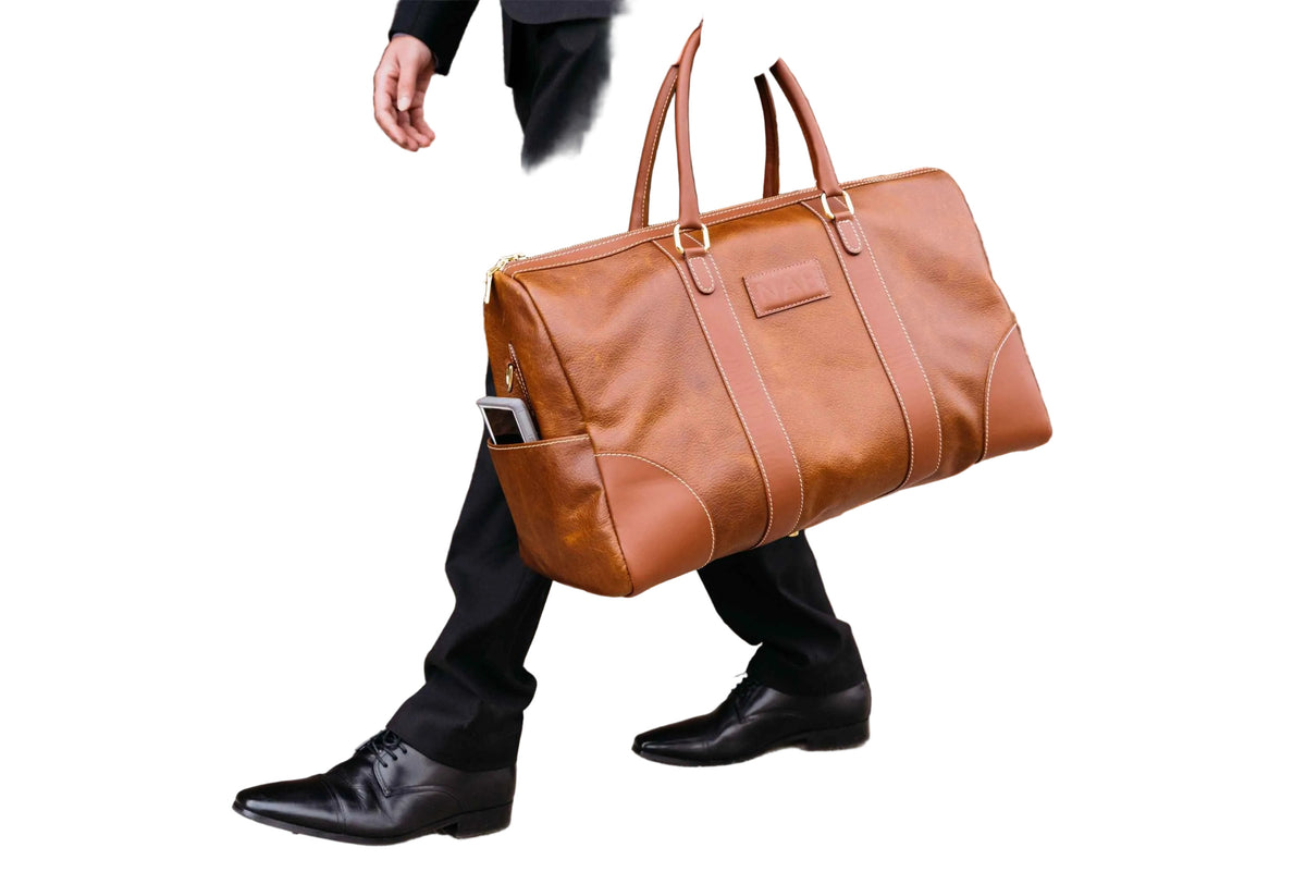 "Person walking with The Shield Duffle in cognac at their side — full-grain leather travel duffle bag made in Canada by NAB Leather"