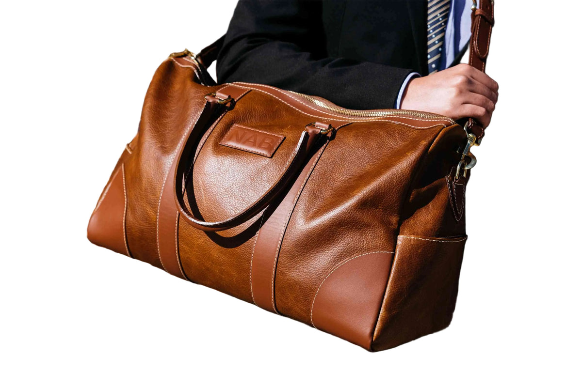 "Cognac Shield Duffle carried by the rolled leather handles — full-grain leather travel bag made in Canada by NAB Leather"