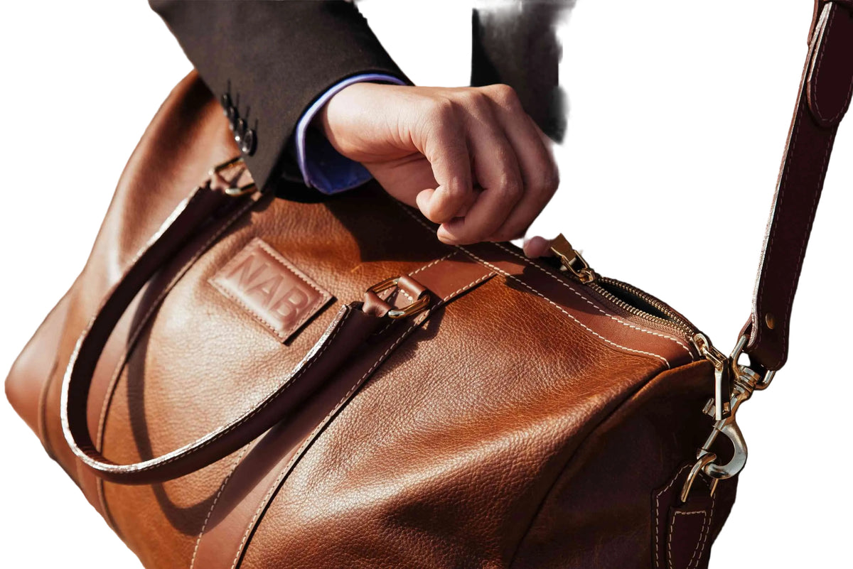 Brown leather duffel bag with a visible brand logo, held by a person in a suit.