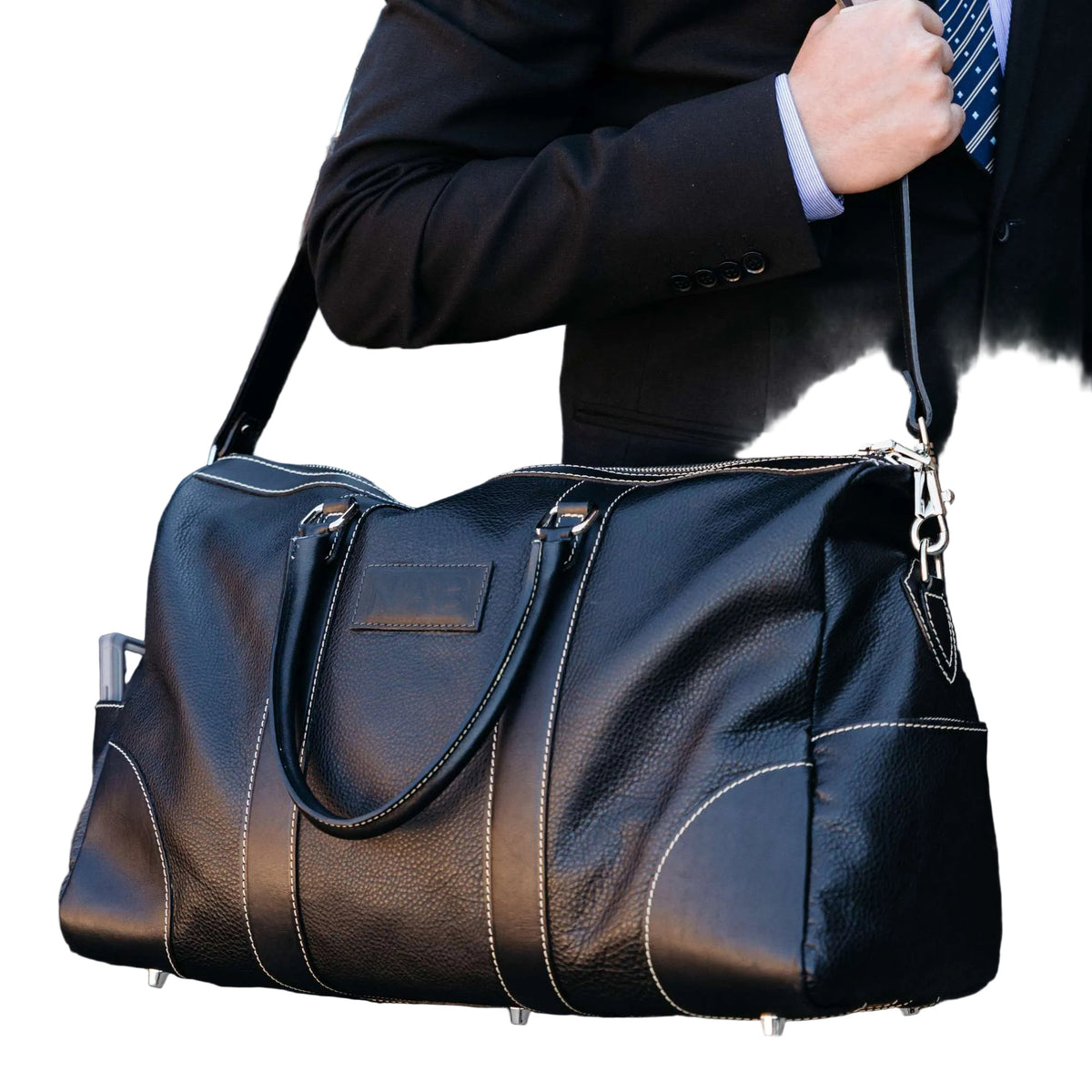 "Person in a suit carrying The Shield Duffle in black by the rolled leather handles — premium full-grain leather duffle bag made in Canada by NAB Leather"
