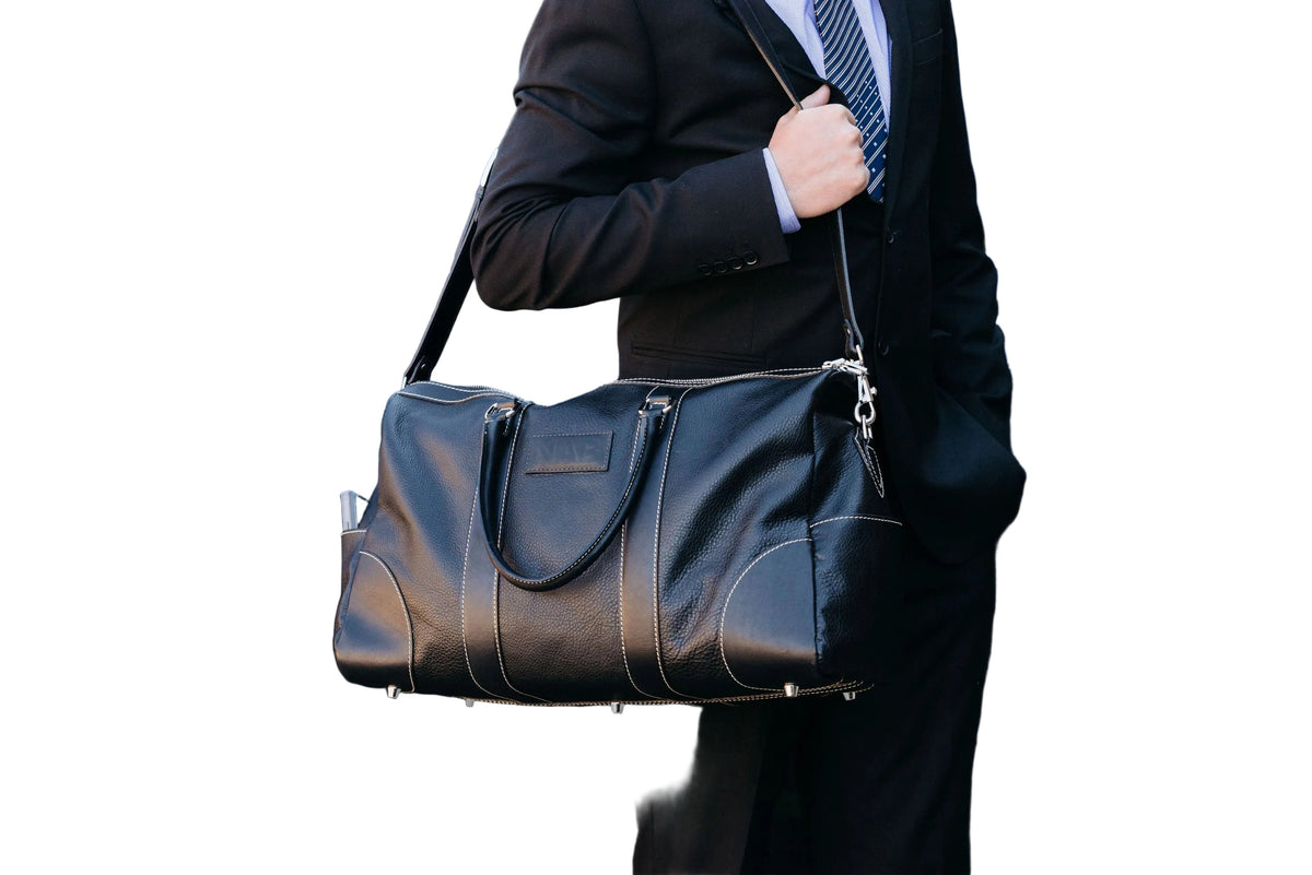 "Person in a suit carrying The Shield Duffle in black by the handles — premium full-grain leather duffle bag made in Canada by NAB Leather"