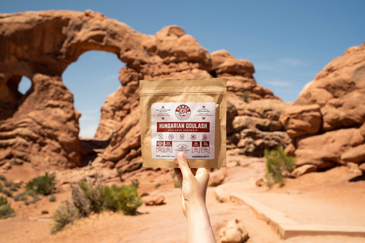 Hand holding a package labeled 'Hungarian Goulash' against a desert landscape with rock formations.