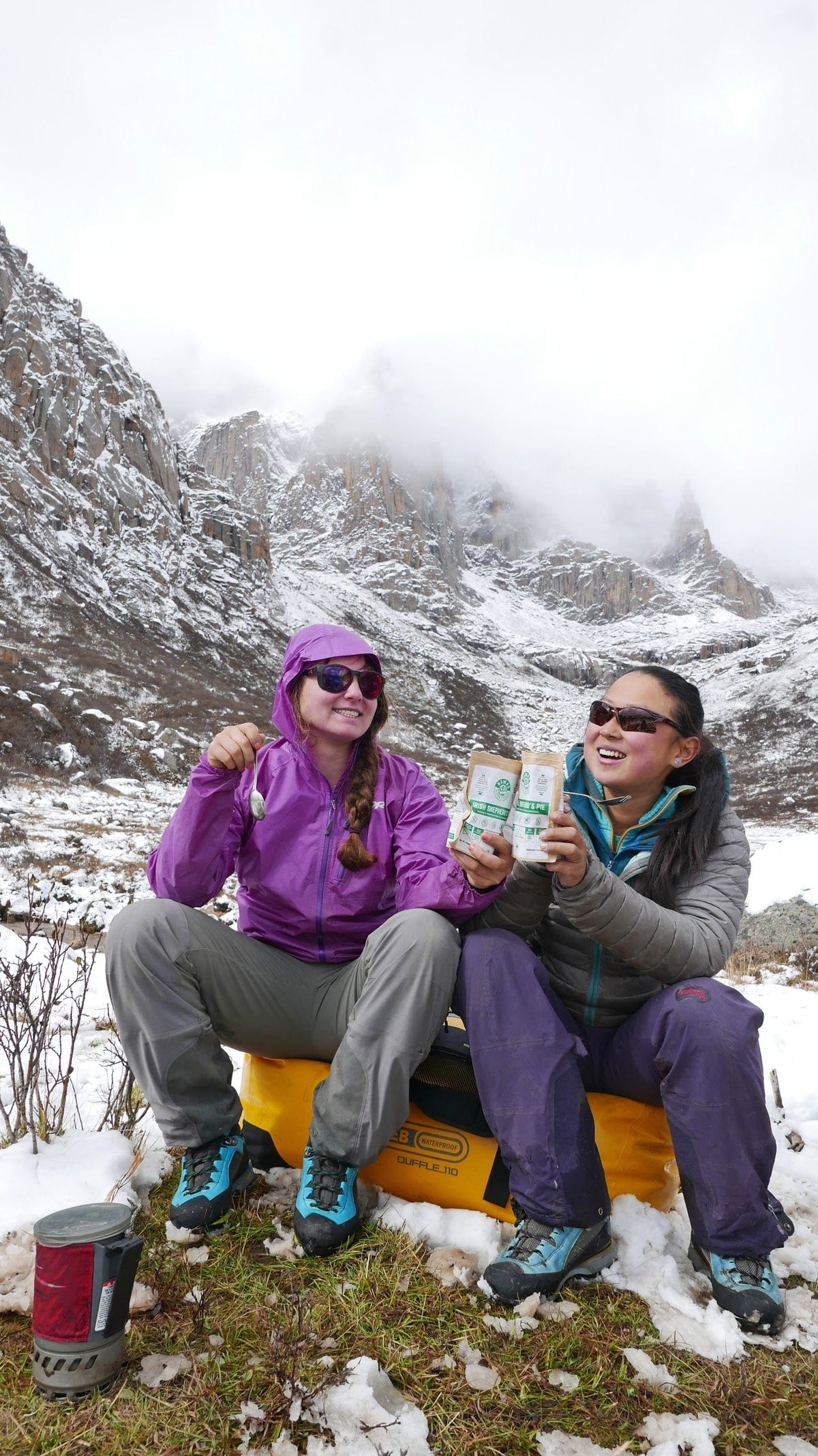 Two people sitting on a tire in a snowy mountain landscape