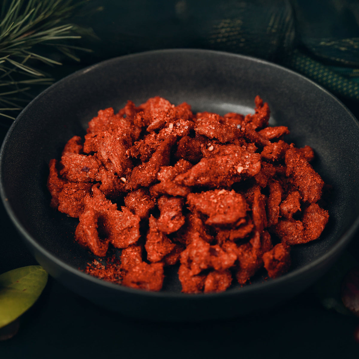 Red snack food in a black bowl with greenery in the background